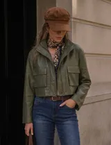 Chaqueta corta de eco cuero color verde militar, con cuello alto, cierre frontal con botones a presión y bolsillos frontales con solapa.