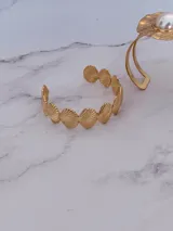 Brazalete abierto de acero dorado, compuesto por dijes con forma de conchas marinas unidas entre sí.
