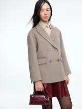 Chaqueta de paño color beige, de corte amplio y diseño cruzado con botones frontales. Presenta solapas clásicas y bolsillos laterales con solapa.