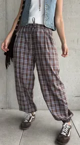Pantalón babucha de corte holgado, con estampa de cuadros en tonos marrón y celeste, cintura elástica con cordón ajustable y puños fruncidos en los tobillos.