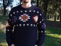 Sweater de lana azul marino con cuello redondo y diseño de copos de nieve y flores en tonos blanco, rojo y violeta. Tejido a mano.