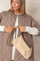 Cartera de gamuza color beige con correa ajustable de cuero sintético marrón, bolsillo frontal con solapa y cierre superior.