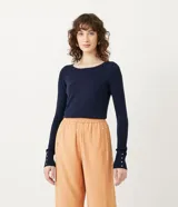 Suéter de punto color rosado, con cuello barco, mangas largas y puños con botones decorativos. El dobladillo también es acanalado.