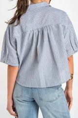 Camisa de manga corta con patrón de rayas verticales en tonos azul y blanco, cuello camisero y cierre frontal con botones.