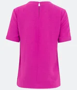 Blusa blanca de poliéster con cuello redondo, mangas cortas, cierre trasero en forma de gota, pequeñas aberturas laterales y acabados en pespuntes en las mangas y el cuello.