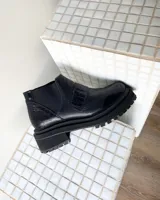 Botineta de cuero vacuno color negro con suela track de goma. Presenta una combinación de texturas en el cuero, incluyendo paneles con efecto croco en el talón y en la tira decorativa sobre el empeine, además de paneles laterales elásticos.