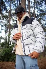 Campera puffer con diseño bicolor, presentando una parte superior en negro y el resto en blanco con estampado tipográfico de la marca. Posee cuello alto, cierre frontal completo y puños elásticos.