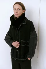 Campera negra con cuello alto de piel sintética, mangas de denim y cuerpo de tela texturizada con pespuntes blancos. Tiene cierre frontal con botones y bolsillos de parche con solapa.