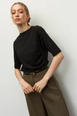 Remera negra de cuello redondo y manga tres cuartos, confeccionada en tela con textura sutil. Presenta fruncidos laterales que aportan caída y movimiento a la prenda.