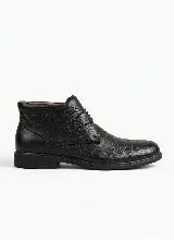 Bota corta tipo botineta de cuero negro con textura granulada, cierre mediante cordones y suela plana de goma.
