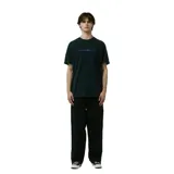 Remera de algodón color verde oscuro/negro con efecto lavado, corte holgado y estampado frontal pequeño con texto y símbolos en color azul.