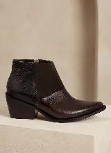 Bota corta de cuero vacuno en color marrón, con diseño de paneles combinados que incluyen textura de reptil en el talón, gamuza en el lateral y cuero liso en la puntera. Presenta un taco cuadrado de 6 cm y suela de caucho antideslizante.