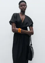 Vestido largo de color negro con cuello en pico y mangas cortas. Presenta un panel fruncido en la cintura que define la silueta y un diseño recto. Confeccionado en una mezcla de lino y ramio con forro de algodón.