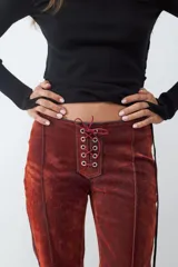 Pantalón de denim con acabado flocked que le otorga una textura aterciopelada, de tiro medio y corte flare. Presenta un cierre frontal con cordones y ojales metálicos, costuras verticales decorativas y paneles laterales en contraste.