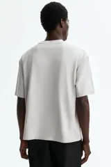 Remera boxy de punto de algodón pesado, color gris claro, con cuello redondo ribeteado acanalado, hombros caídos y mangas cortas de corte holgado.