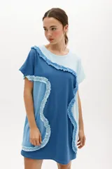 Vestido corto de algodón con diseño de bloques de color en tonos azul y celeste. Presenta un corte relajado, cuello redondo, mangas cortas y detalles de volados aplicados en forma curva a lo largo de la prenda.