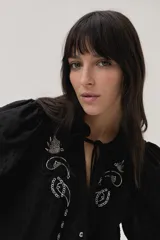 Blusa blanca con lunares en relieve, cuello con volados y lazos, mangas abullonadas 3/4 y bordados con lentejuelas en el frente.