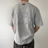 Remera oversize gris con efecto lavado, de manga corta y cuello redondo. Presenta un gran diseño bordado en la espalda con el contorno de una estrella y letras superpuestas.