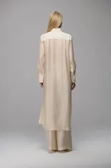 Camisa larga semitransparente de diseño fluido, con cuello clásico, mangas largas con puños anchos y detalle de nervaduras verticales en el frente. Presenta una caída ligera y sofisticada.