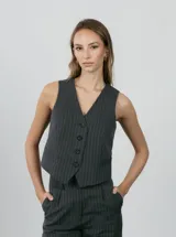 Chaleco sastrero gris oscuro con finas rayas verticales blancas, escote en V y cierre frontal con cuatro botones.