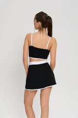 Conjunto deportivo de dos piezas compuesto por un top de tirantes finos con detalle de ribete blanco y logo estampado, y una pollera short con cintura elástica blanca y tajo lateral con ribete blanco.