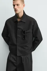 Sobrecamisa de corte relajado, color negro, con cuello solapa, cierre frontal de botones, mangas largas con puños abotonados y bolsillos de plastrón en el pecho.