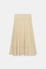 Falda larga de tiro medio en color beige, con tejido de textura cuadriculada. Presenta un diseño acampanado con detalle de costura horizontal y bajo acabado en volante. Cierre lateral con cremallera oculta.