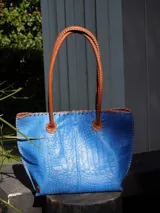 Bolso shopper de cuero azul con textura crocco, manijas largas marrones y costuras artesanales visibles en los bordes.
