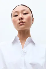 Camisa blanca de manga larga con cuello clásico y botones frontales ocultos.