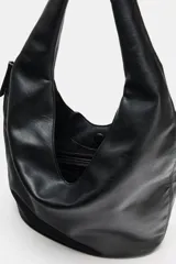 Bolso de hombro tipo saca en formato maxi, confeccionado en material sintético con acabado liso. Cuenta con asa única para llevar al hombro, cierre imantado en el compartimento principal, bolsillo lateral con cremallera y bolsillo interior con cierre.