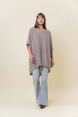 Maxi sweater tejido color beige con efecto metalizado sutil, silueta amplia, mangas tipo murciélago y largo asimétrico (más corto adelante y más largo atrás).