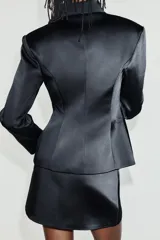 Falda mini de tiro bajo confeccionada en tejido satinado negro, con cierre lateral con cremallera oculta.