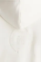 Campera con capucha de algodón pesado, color blanco hueso, de corte holgado y hombros caídos. Posee cierre frontal bidireccional, bolsillos canguro delanteros y puños y bajo acanalados.