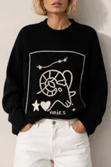 Sweater negro de punto con bordados artesanales en tono crudo que representan el signo del zodíaco Aries, con cuello redondo y diseño oversize.