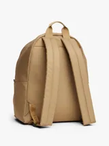 Mochila de diseño redondeado color beige, con compartimento principal y bolsillo frontal con cierre. Incluye parche con logo de la marca en la parte inferior, asa superior y correas acolchadas ajustables.
