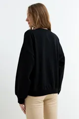 Buzo negro con efecto lavado, cuello redondo y manga larga. Presenta un diseño estampado en relieve con forma de corazón y la inscripción "Good Mood" en el centro.