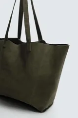 Bolso tipo shopper de piel con acabado serraje, color verde militar. Cuenta con dos asas de mano y un bolsillo interior con cierre de cremallera.