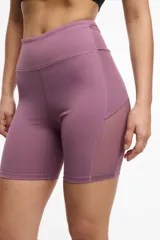 Short deportivo tipo biker de cintura alta, color violeta, con paneles laterales de microtul y bolsillos integrados.