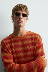 Jersey relaxed fit de punto calado con rayas horizontales en tonos naranja y amarillo. Tiene cuello redondo y manga larga con acabados irregulares.