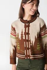 Cardigan de punto color crudo con detalles en marrón oscuro. Presenta cuello redondo, cierre frontal con botones tipo alamares y puños y ruedo acanalados con rayas horizontales. Incluye un pequeño aplique bordado en la manga.