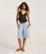 Bermuda jorts de denim color celeste claro, de tiro medio con cinco bolsillos, trabillas para cinturón y cierre frontal con botón y cremallera.
