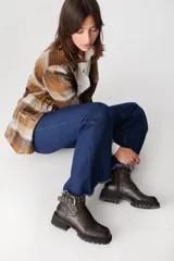 Bota corta de cuero color chocolate con suela track, cierre lateral y correa decorativa con hebilla metálica y tachas en el tobillo.