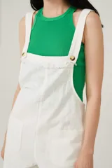 Enterito corto blanco con breteles anchos, escote recto con detalle de flecos y bolsillos delanteros.