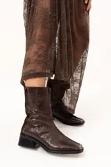 Bota de caña media con textura de reptil, confeccionada en cuero color chocolate. Presenta puntera cuadrada, taco bloque y cierre lateral interno.
