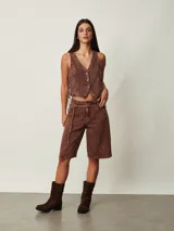 Top estilo chaleco crop de denim marrón con efecto acid wash, escote en V, cierre frontal con botones metálicos y cordones ajustables en los laterales.