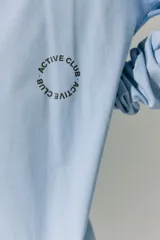 Remerón de manga larga color celeste, con cuello redondo y puños acanalados. Presenta una estampa circular en la espalda con el texto 'ACTIVE CLUB' y detalles de texto adicional en la parte inferior.