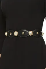 Cinto negro de cuero sintético con apliques de perlas sintéticas y detalles metálicos dorados.