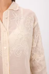 Camisa de encaje color crema con diseño floral bordado, cuello camisero, cierre frontal con botones y mangas largas con terminación acampanada.