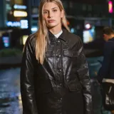 Campera de poliuretano color negro, de diseño liso con cuello camisero, cierre frontal con botones y múltiples bolsillos delanteros con solapa y botón.