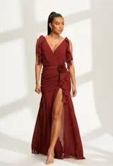 Vestido largo de fiesta color bordó, con escote en V, mangas cortas con volados en los hombros, cintura fruncida con detalle de flor aplicada y falda con tajo lateral profundo.